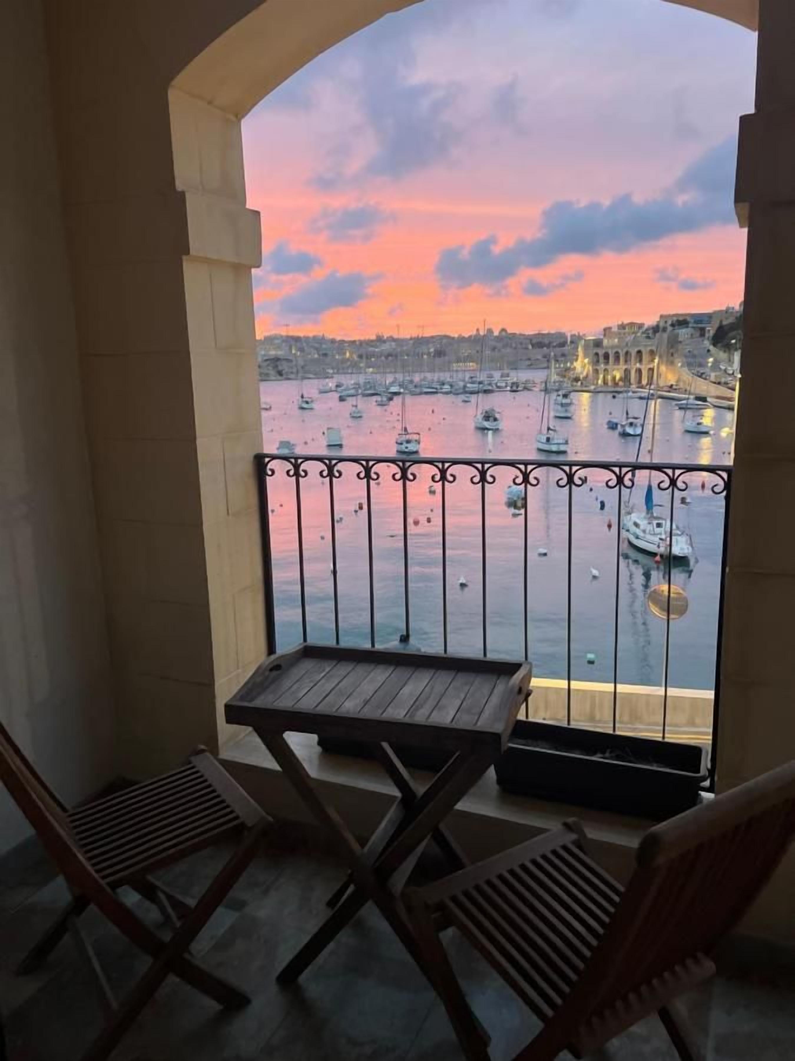 Un balcón con vista a un puerto al atardecer, con barcos y un puente.