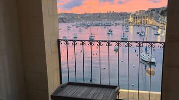 Un balcón con vista a un puerto al atardecer, con barcos y un puente.