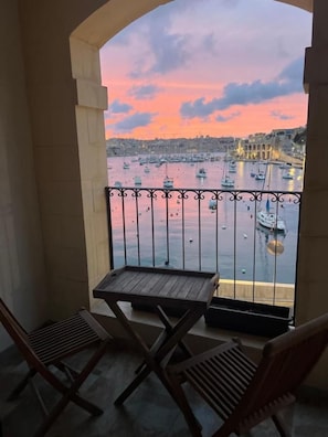 Un balcón con vista a un puerto al atardecer, con barcos y un puente.