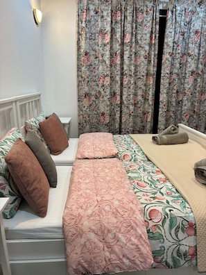 Un dormitorio con cama, almohadas, mesita de noche y cortinas.