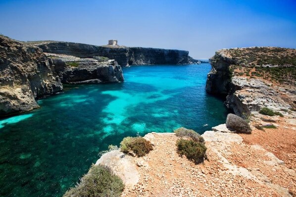 A coastal landscape with rocky terrain and clear blue waters. - Front Row Malta - Waterfront Home    (Il-Kalkara)