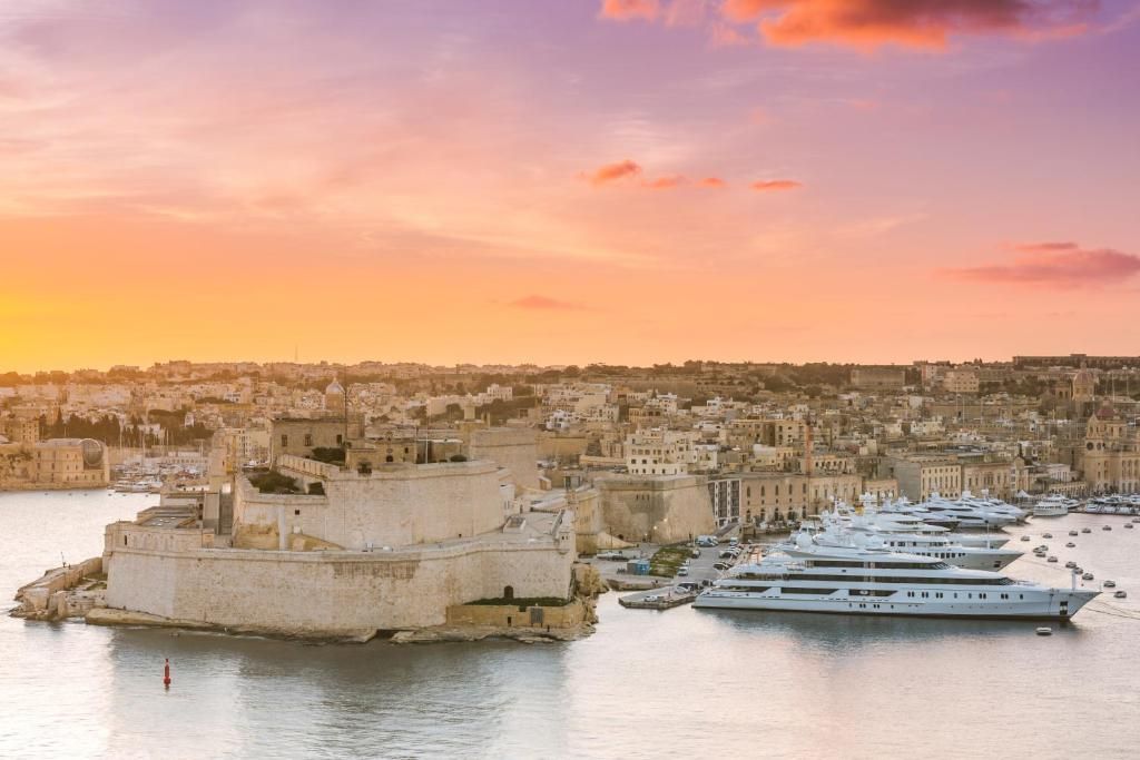 Un paysage urbain côtier avec une structure fortifiée imposante et une marina où sont amarrés de nombreux yachts.