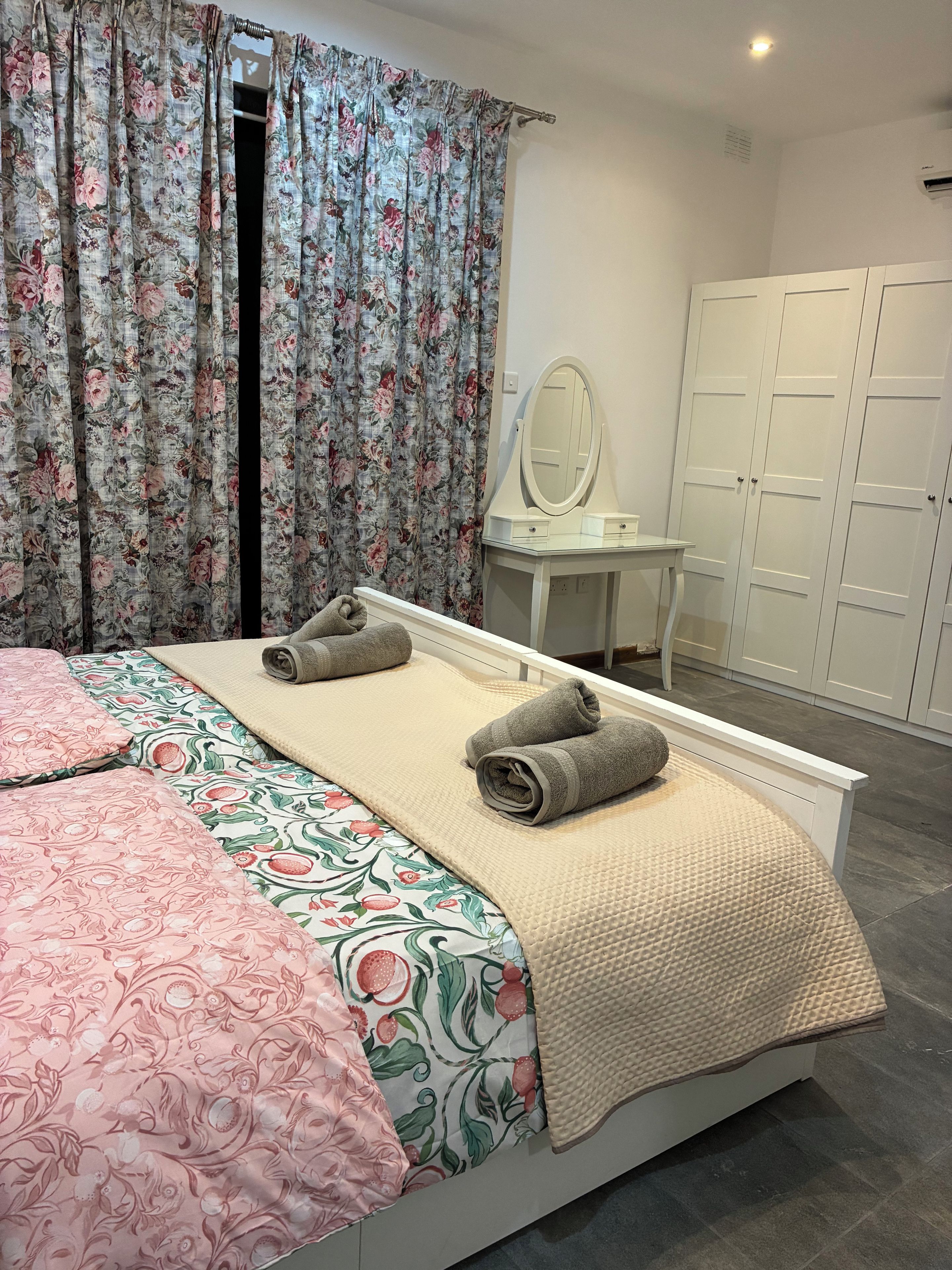 Una cama bien hecha con un edredón estampado de flores, una colcha color beige y dos toallas enrolladas.