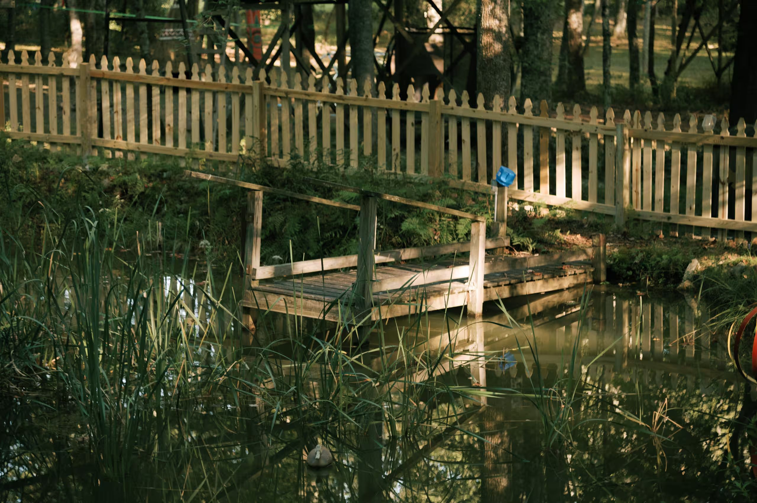 A wooden bridge over a body of water with a fence in the background.