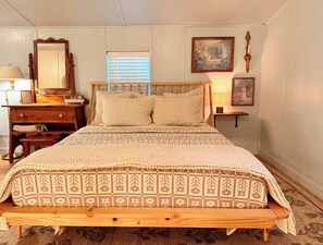 Een slaapkamer met een houten bed, een dressoir, een spiegel en wandlampen.