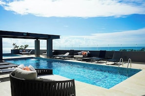 A rooftop pool area with lounge chairs and a view of the ocean. - Modern Condo: Rooftop Pool, Gym, Walk to Beach (Playa del Carmen)