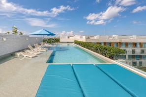 A rooftop pool with lounge chairs and a blue umbrella, surrounded by buildings. - Modern Playa del Carmen Apt: Rooftop Pool & Wifi (Playa del Carmen)