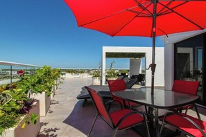 Eine Außenpatio mit Glastrennwand, roten Stühlen, einem runden Tisch und einem roten Sonnenschirm.