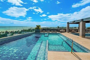 A rooftop infinity pool with a clear view of the ocean, lounge chairs, and a covered seating area. - Ocean-view Condo - Rooftop Infinity Pool & Wifi (Playa del Carmen)
