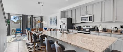 A modern kitchen with a large island, bar stools, and a dining area with blue chairs.