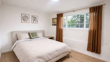 A bedroom with a bed, a nightstand, a window with curtains, and wall art.