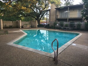Piscina retangular com uma escada metálica no centro, rodeada por um deck de concreto.