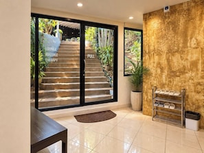 A modern interior with a staircase leading to a garden, a wooden bench, a shoe rack, and a textured wall. - Smith & Appy Hillside Seaview Hostel (Chang Wat Surat Thani)