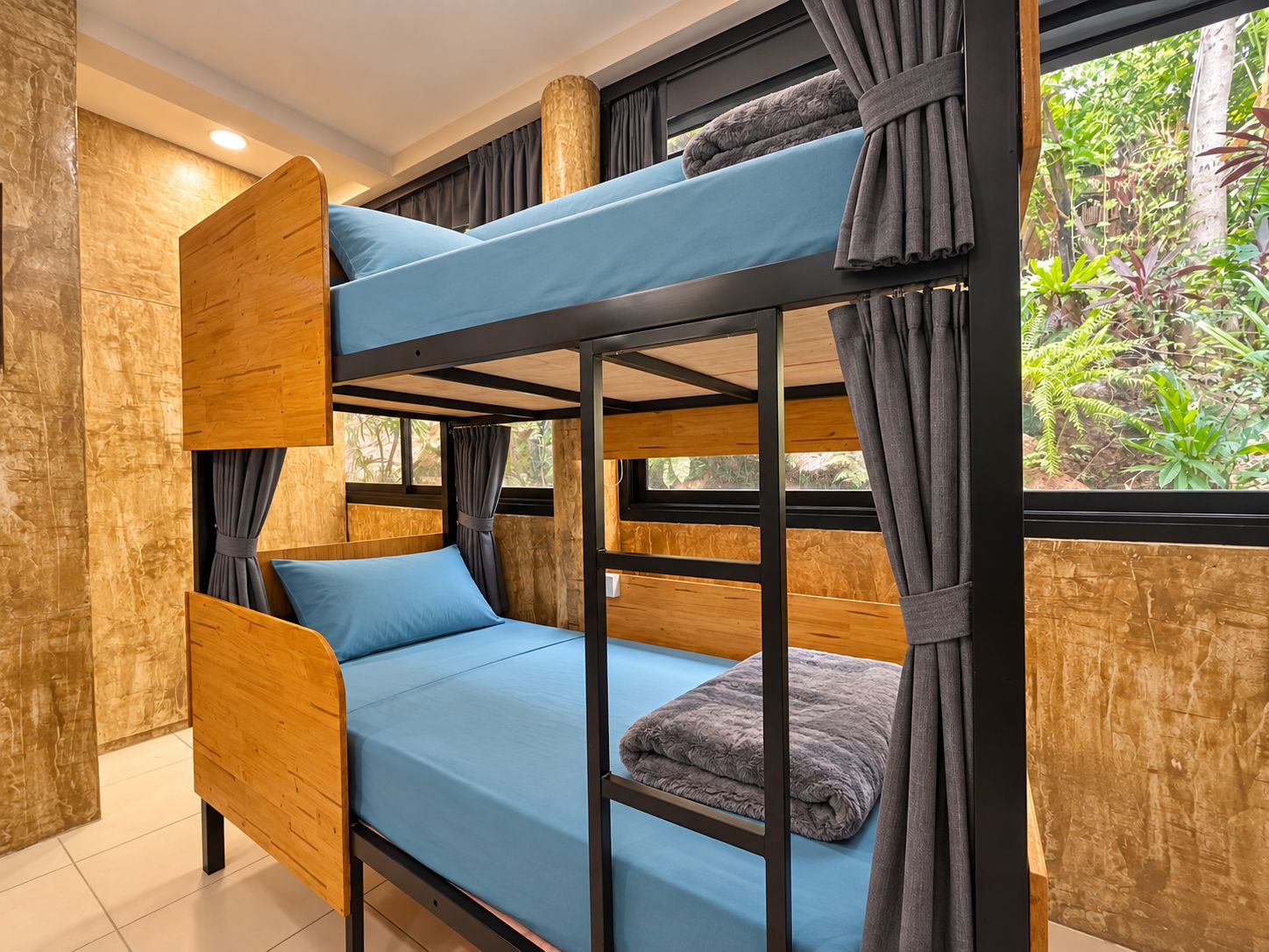 Una cama litera con colchón azul, almohadas grises y cortinas.