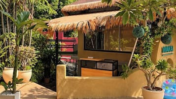 A thatched-roof structure with a small seating area and a potted plant nearby.