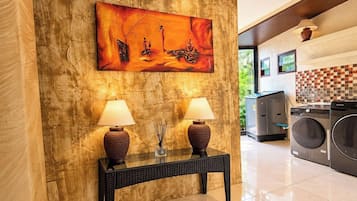 Vestíbulo de hotel con un cuadro abstracto grande, dos lámparas sobre una consola y un área de lavandería con lavadoras.