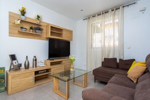 A living room with a flat-screen TV, wooden entertainment unit, glass coffee table, brown sofa, and a window with curtains. - CH Villa Macarena La Marquesa Golf (Ciudad Quesada)