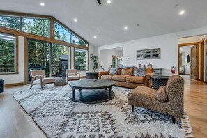 A spacious living room with a large window, a round coffee table, leather sofas, and a patterned rug. - Tahoe Vista Sanctuary | Hot Tub + Fireplace (Tahoe Vista)