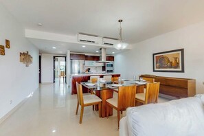 A modern kitchen with a dining area, white walls, and a wooden dining table. - Playa Condo: Beach, Pool, & Family Fun! (Playa del Carmen)
