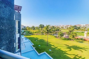 A hotel room with a view of a swimming pool, a grassy area, and palm trees. - Playa Condo: Beach, Pool, & Family Fun! (Playa del Carmen)