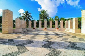 A courtyard with a patterned floor, palm trees, and stone pillars. - Playa Condo: Beach, Pool, & Family Fun! (Playa del Carmen)