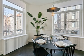 A dining area with a table set for four, large windows, and a potted plant. - SUDANVERS (Antwerpen)