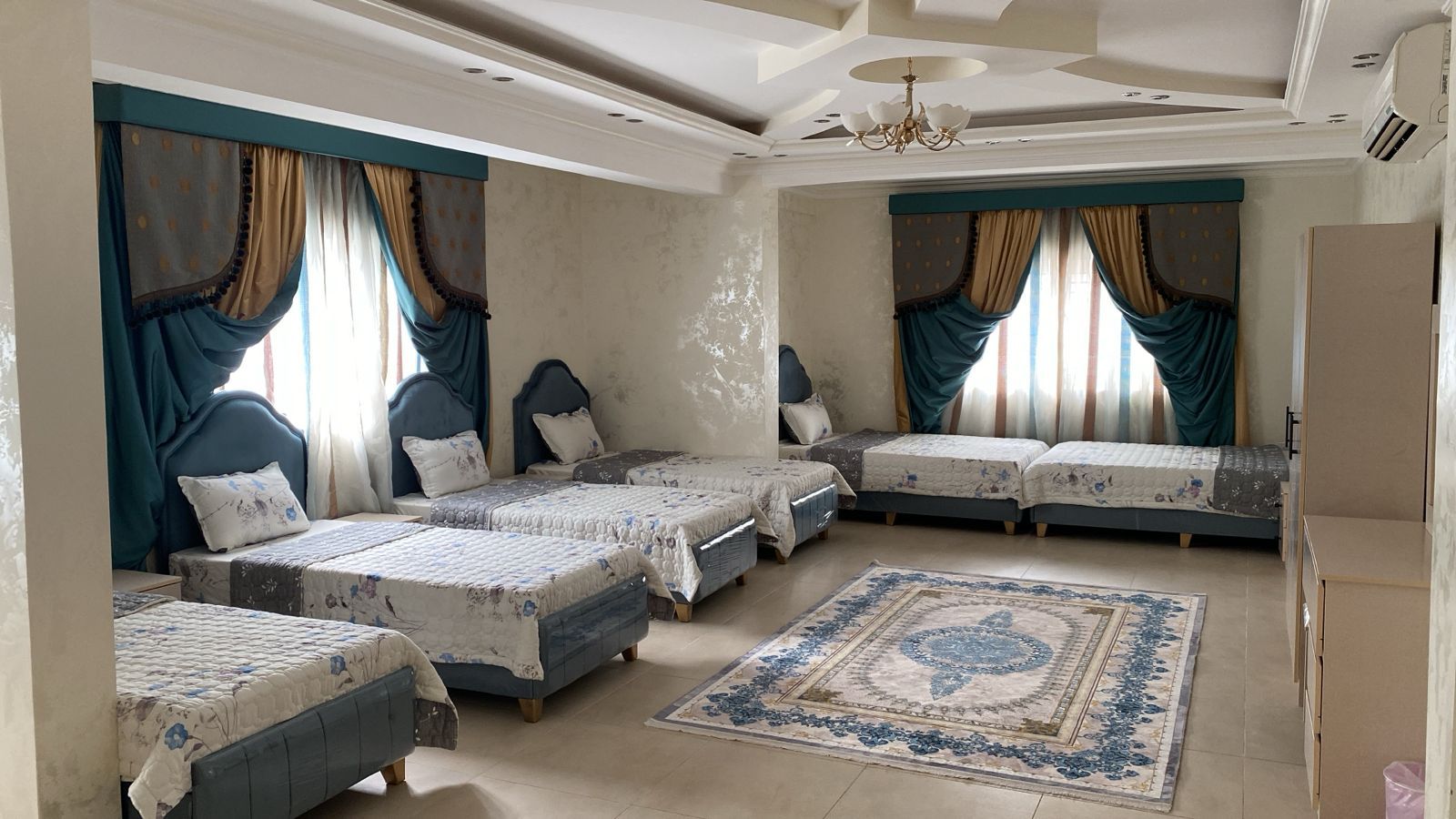 Une chambre à coucher avec plusieurs lits, un lustre et un tapis à motifs.