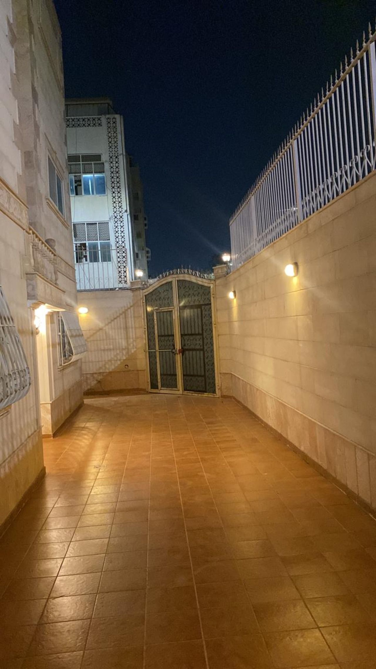 Un couloir doté d’une entrée fermée par un portail, d’un sol carrelé et de murs équipés de luminaires.