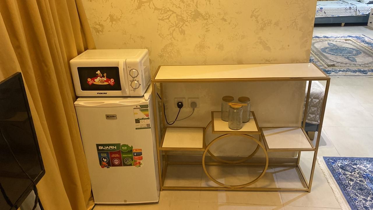 Une petite cuisine équipée d’un four à micro-ondes, d’un réfrigérateur et d’une petite étagère avec des bocaux.