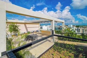 A rooftop terrace with a white structure, outdoor seating, and a view of the cityscape. - Playa del Carmen Condo Rooftop Pool & Balcony (Playa del Carmen)