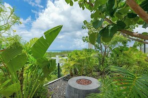 A garden with a circular stone feature surrounded by tropical plants and a view of the ocean. - Playa Studio Rooftop Pool & Balcony (Playa del Carmen)