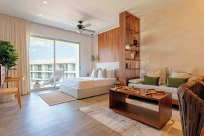 A modern hotel room with a bed, sofa, coffee table, and a balcony with a view. - Playacar 1BR Resort Pool & Dog-friendly (Playa del Carmen)