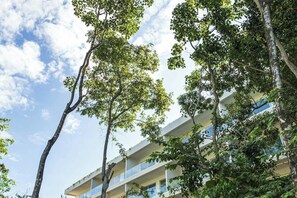A multi-story building with balconies, surrounded by trees. - Playacar Accessible Condo - Pools - Sleeps 7 (Playa del Carmen)