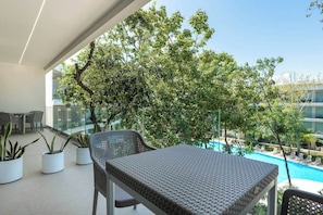 A balcony with a table and chairs, potted plants, and a view of a swimming pool and buildings. - Playacar Condo - Balcony - Pools - Sleeps 6 (Playa del Carmen)