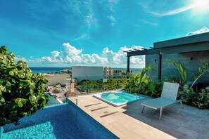 A rooftop pool area with a view of the ocean, a lounge chair, and a pergola structure. - Studio Rooftop Pool & Gym, Steps to Beach (Playa del Carmen)