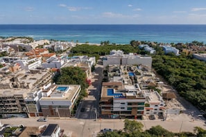 An aerial view of a coastal urban area with buildings, roads, and a beach. - Stylish 1BR Condo: Beach, Rooftop Pool & 5th Ave (Playa del Carmen)