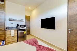 A hotel room with a bed, a TV mounted on the wall, a kitchenette with a microwave, and a wooden door. - Stylish Studio Near Akumal - Rooftop Pool & Wifi (Akumal)