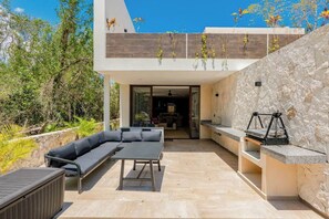 An outdoor patio with a sofa, table, and grill area, surrounded by stone walls and vegetation. - Xpu-ha Beachfront Villa 1: Private Pool & Gym (Xpu-Ha)