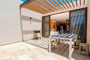 A modern outdoor patio with a table and chairs, a grill, and a sliding glass door leading to a kitchen. - Xpu-ha Villa Private Jacuzzi & Beach (Xpu-Ha)