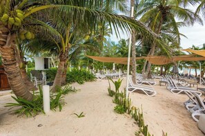 A beachside area with palm trees, lounge chairs, and a small structure. - Xpu-ha Villa Private Jacuzzi & Beach (Xpu-Ha)