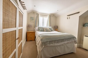Ein Schlafzimmer mit Bett, Nachttisch, Schminktisch, einem Fenster mit Vorhängen und einer Heizung.
