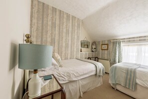 Une chambre avec deux lits, une table de chevet avec une lampe, un miroir et une fenêtre avec des rideaux.