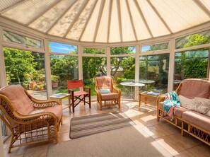 Une véranda meublée de mobilier en osier, dotée de grandes fenêtres et offrant une vue sur le jardin.