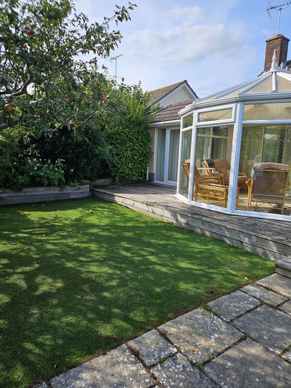 Un jardin bien entretenu, avec une pelouse, une terrasse en bois et une véranda meublée de meubles en osier.