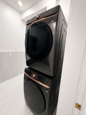 Eine nebeneinander geschaltete Waschmaschine und ein Trockner in einem modernen, minimalistischen Raum mit weißen Wänden und einem hellen Boden.