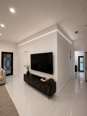 Ein modernes Wohnzimmer mit einem großen Flachbildfernseher, der an einer schwarzen Konsole befestigt ist, einem beigen Sofa und einem minimalistischen Design.