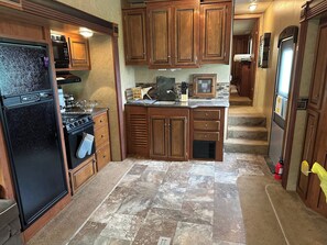 A compact kitchen with wooden cabinets, a black refrigerator, a stove, and a microwave. - Renegade Ranch and Hunt Club – Site 4 (St George)