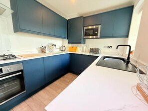 A modern kitchen with dark blue cabinets, a white countertop, a built-in oven, a microwave, a toaster, and a sink with a black faucet. - 3 Seascapes
A bright and modern apartment with lovely views towards Swanage Bay. (Swanage)