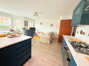 A modern kitchen with a gas stove, a dining area with a white table and chairs, and a living room with a sofa and a television. - 3 Seascapes
A bright and modern apartment with lovely views towards Swanage Bay. (Swanage)