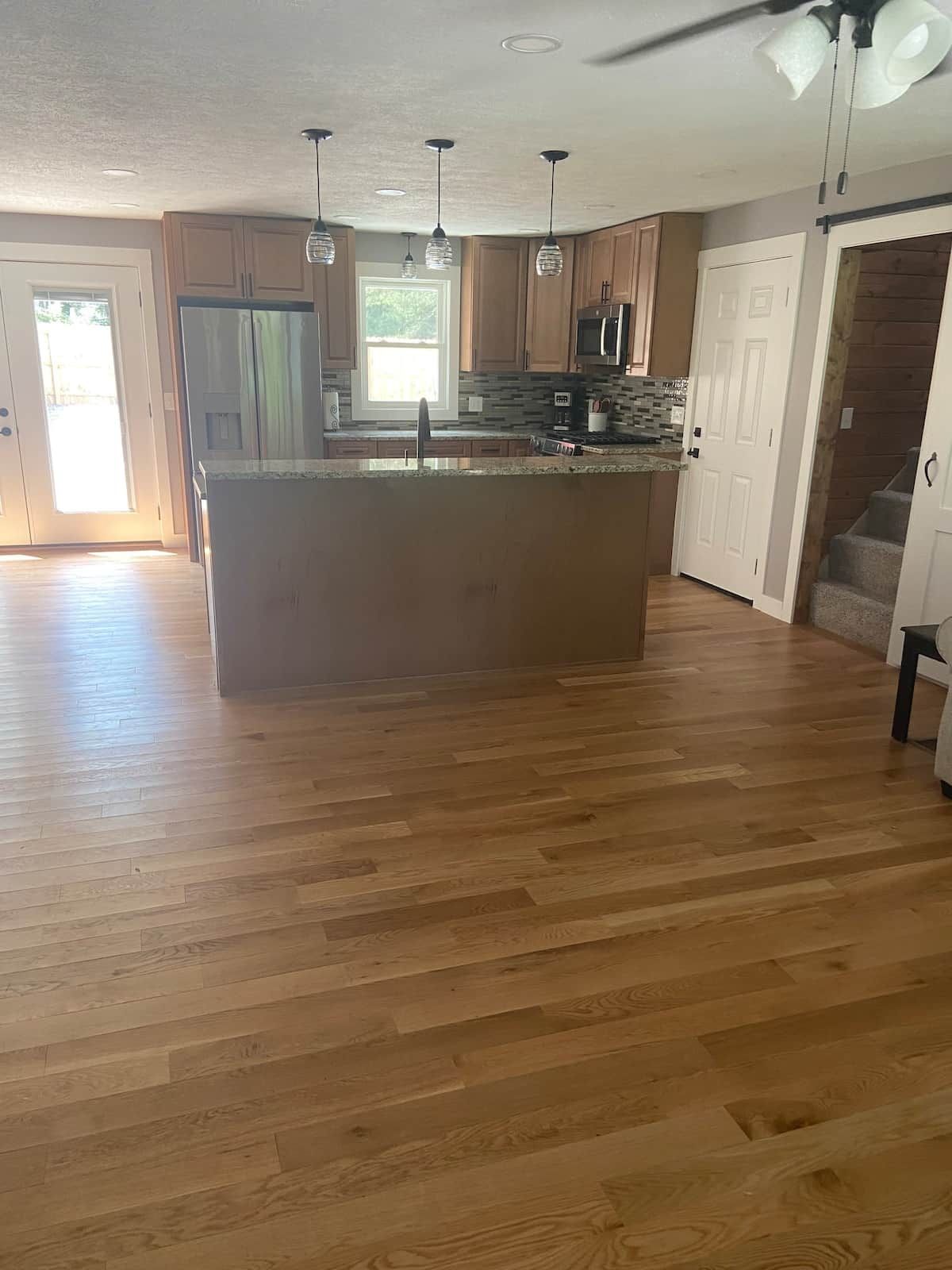 Une cuisine spacieuse avec un grand îlot central, un plancher en bois et des luminaires suspendus.
